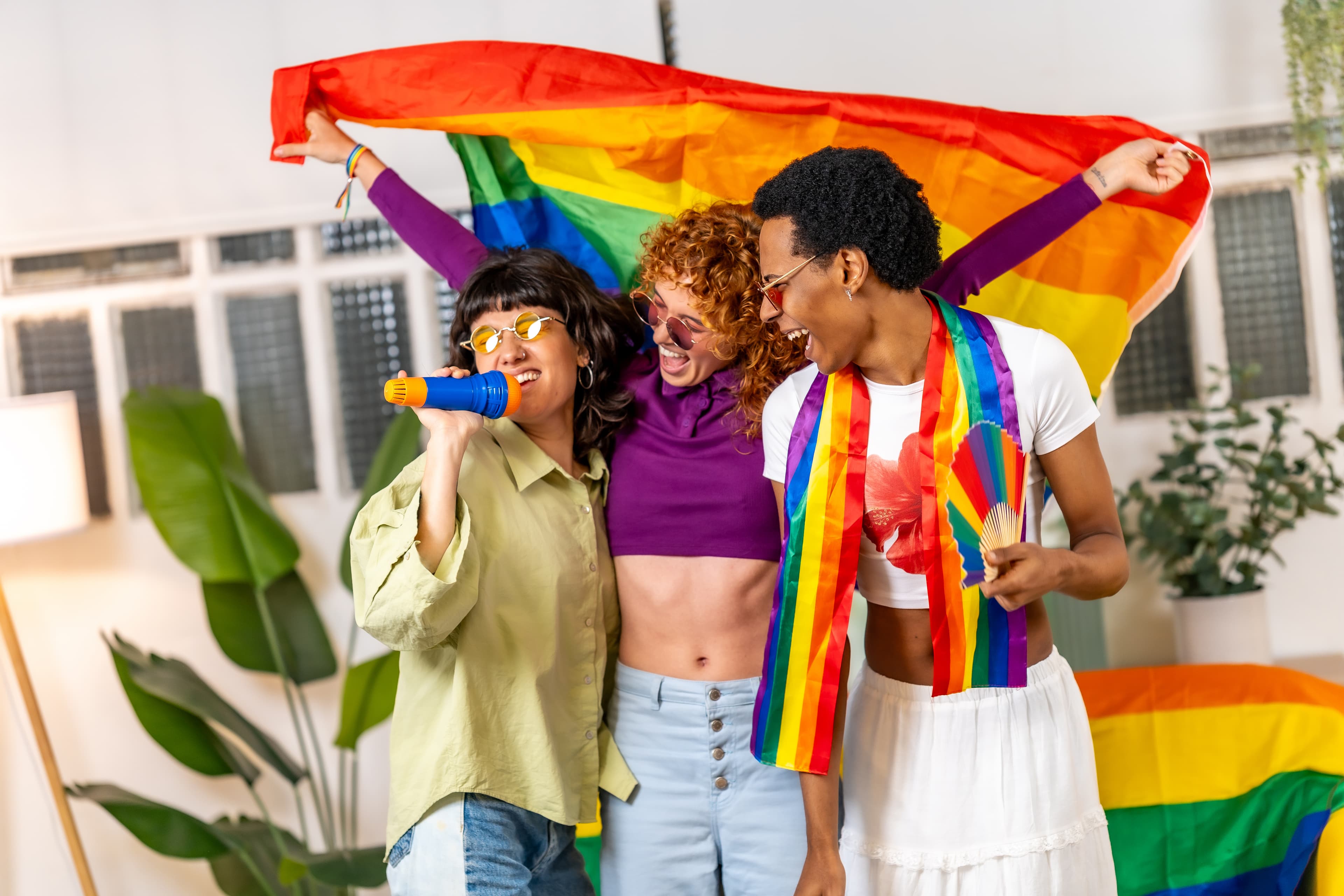 Pessoas celebram a diversidade segurando uma bandeira arco-íris em um ambiente interno. A cena destaca inclusão, respeito e orgulho LGBTQIAP+.