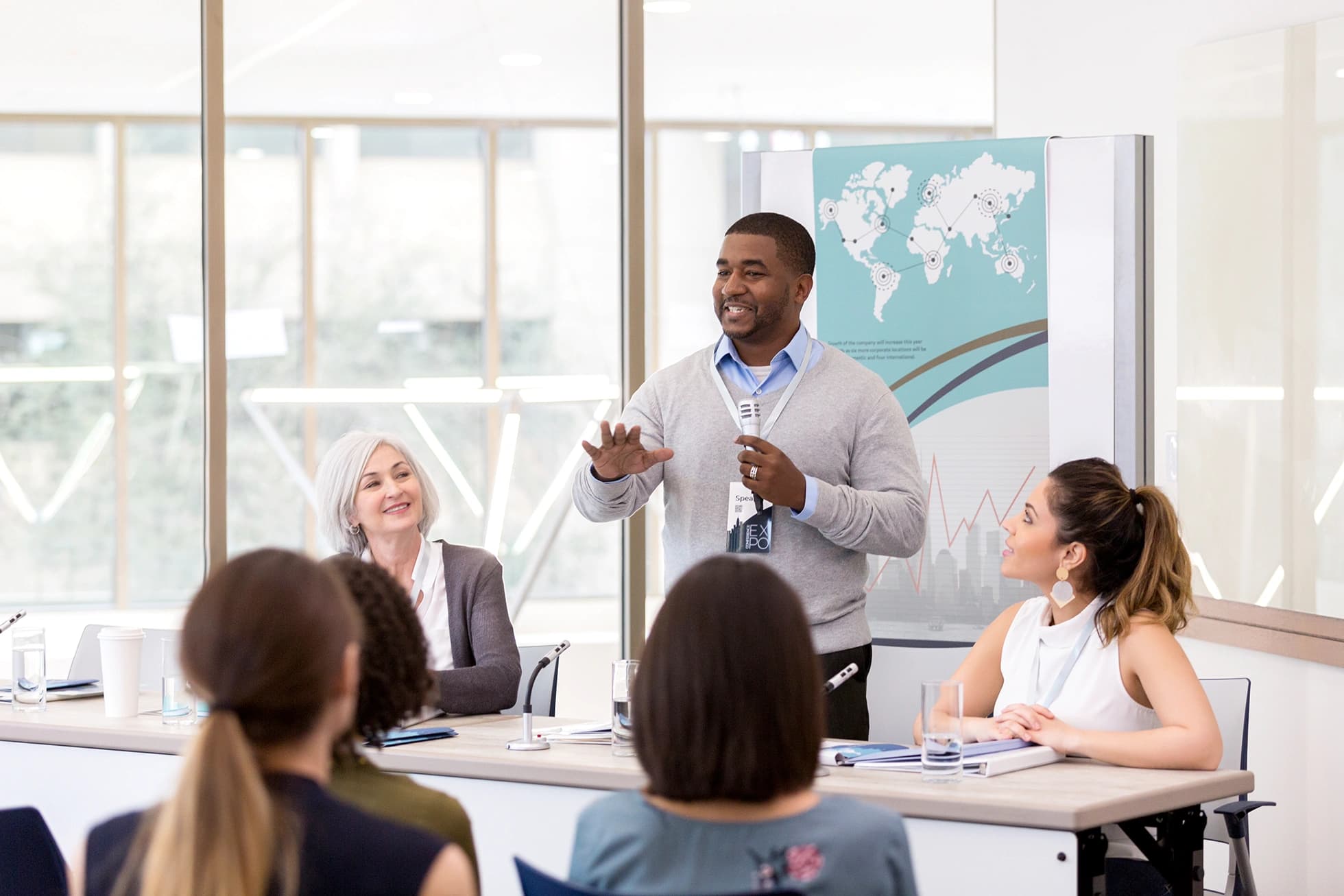 Young african man talking to a group of people sitting at a table.