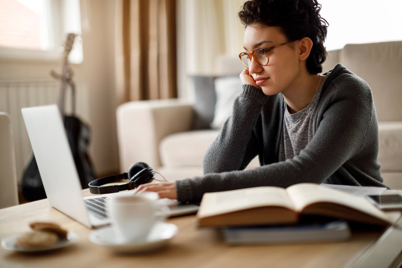 A young female student sitting at a desk using her laptop with some books open.