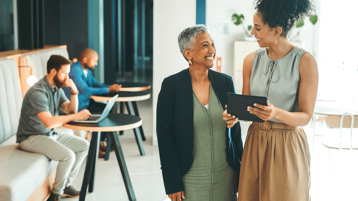 Dos profesionales conversan en una oficina mientras consultan una tableta, representando apoyo, bienestar y acceso a recursos para empleados.