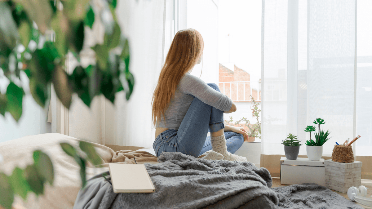 Una persona seduta vicino a una finestra si prende un momento di pausa, rappresentando recupero, benessere e gestione dello stress estivo.